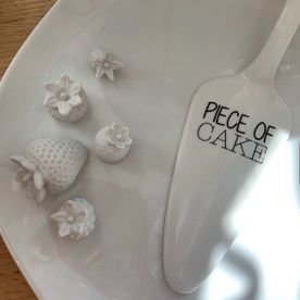 Tortenheber mit Schriftzug "Piece of Cake" auf einem Teller mit Fruchtdekoration
