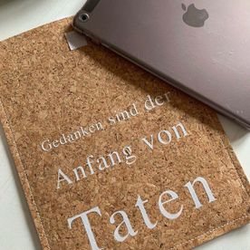 Notizbuch in Korkoptik mit weißem Schriftzug, darauf ein Apple-Produkt