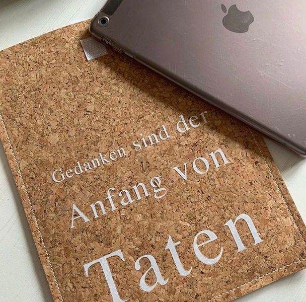 Notizbuch in Korkoptik mit weißem Schriftzug, darauf ein Apple-Produkt